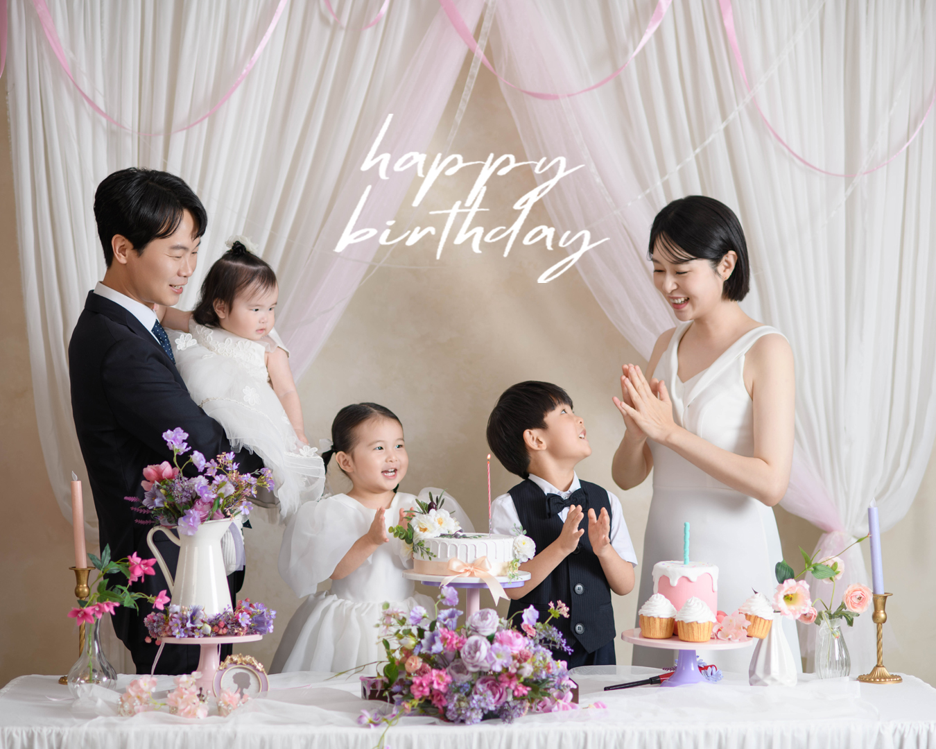 꽃과 케이크가 놓인 돌상 앞에서 아이의 생일을 축하하는 가족